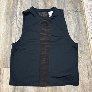 Svart ärmlös linnetopp Puma x Kenza - Säljer en svart ärmlös linnetopp från Puma x Kenza i storlek XS. Toppen har en meshpanel framtill med broderad Puma-logga och rund halsringning. Snygg och sportig design som passar perfekt till träning eller en chill look.