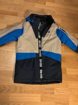 8848 Altitude blå och beige skidjacka  - Säljer en snygg skidjacka från 8848 Altitude i färgerna blå, beige och mörkblå. Jackan har huva, dragkedja med logga och praktiska fickor. Perfekt för dig som vill ha en sportig look i backen.