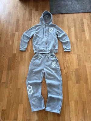 Grå tracksuit - Tjena! Jag säljer en snygg grå tracksuit med vitt tryck i storlek XS/S. Tracksuiten är aldrig använd. Jag köpte den här på plick så jag vet ej vilket märke. Perfekt för dig som vill vara unik. Hör av dig vid funderingar