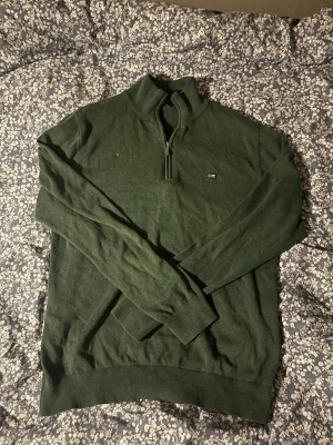 Grön half zip tröja från Lexington - Mörkgrön långärmad tröja från Lexington med half zip och liten logga på bröstet. Tröjan har ribbade muddar och hög krage, perfekt för lager-på-lager. Skön och stilren, passar till det mesta. Lägg gärna bud