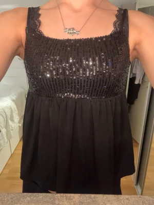 Svart snygg glittertopp!💘 - Snygg svart topp med glittriga paljetter över bysten. Modellen är ärmlös och har en lös, flowy passform nedtill. Perfekt för dig som vill sticka ut lite extra.
