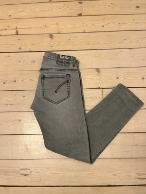 Grå Dondup George jeans - Snygga ljusgrå Dondup jeans i modellen George med slim fit-passform och klassisk femfickssdesign. De är storlek W30 men de sitter mer som W29. Byxorna har svarta detaljer och diskret Dondup-logga samt raka ben. Jeansen är i mycket bra skick utan hål eller defekter. Nypris ca 3000kr. Materialet är mjukt med lite stretch för extra komfort. Perfekt för dig som gillar stilrena och moderna jeans. Vid frågor eller funderingar hjälper jag gärna till Mvh Olof.