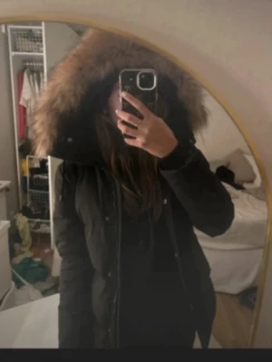 Hollies vinterjacka - Säljer en svart, vadderad vinterjacka i mycket fint skick. Jackan är varm och bekväm, perfekt för kalla höst- och vinterdagar. Den har en huva med mjuk pälsdetalj som både ger extra värme och en stilren look. Jackan stängs med dragkedja och knappar och har praktiska fickor framtill. Figurnära men ändå rymlig, lätt att bära över stickade tröjor.