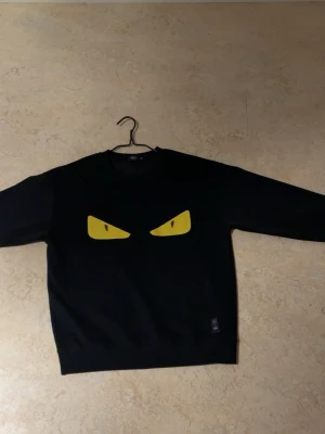 Fendi  sweatshirt - Cool svart sweatshirt från Fendi med stora gula ögon tryckta på bröstet. Tröjan har rund hals och långa ärmar, perfekt för dig som vill sticka ut med en unik och edgy stil. Passar lika bra till jeans som till mjukisbyxor.