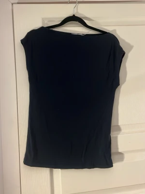 Svart enkel topp med kort ärm - En svart, stilren topp med korta ärmar och rund halsringning. Modellen är figurnära och passar perfekt till jeans eller kjol. Tillverkad i mjukt och lätt material som känns skönt mot huden.