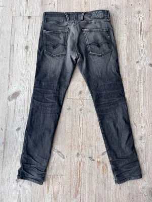 Replay Anbass svarta jeans, W30 L32 - Svarta Replay Anbass jeans med snygg tvättad look och klassiska fem fickor. Slim passform och raka ben, med coola detaljer på bakfickorna. Perfekta för dig som gillar stilrena och moderna jeans.