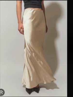 Ljusbeige satinkjol i maxilängd - Supersnygg långkjol i ljusbeige satin-look med mjukt, glansigt material och figurnära passform. Kjolen har en enkel, clean design utan synliga detaljer och faller snyggt längs kroppen. Perfekt till sneakers eller klackar för en trendig vibe.