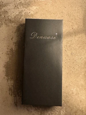 Klocka  - Bilderna visar en silverfärgad armbandsklocka från Denuasi i metall med klassisk länk och datumvisning, samt två små parfymprover Jean Paul och valentino