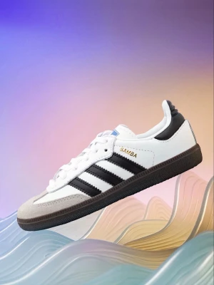 Adidas Samba sneakers vit/svart - Adidas Samba sneakers i klassisk vit och svart färg med guldtext på sidan. Skon har tre svarta ränder, vit ovandel i skinn och mockadetaljer vid tån. Platt svart sula och snörning framtill. Perfekt för dig som gillar retrostil och sportig vibe.