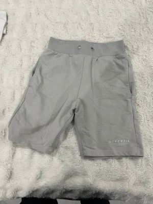 Grå shorts från McKenzie - Säljer ett par ljusgrå shorts från McKenzie med bred transferresår i midjan och två sidofickor. distinct logga på vänster ben. Sk referring till en clean branches look och mjukt bomullsmaterial som är sköna att bära hela dagen.