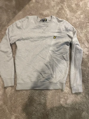 Ljusgrå sweatshirt från Lyle & Scott - Säljer en ljusgrå sweatshirt från Lyle & Scott i storlek S. Tröjan har rund halsringning, ribbade muddar och den klassiska gula örnloggan broderad på bröstet. Perfekt basic som funkar till allt och är riktigt skön tack vare mjukt bomullsmaterial.