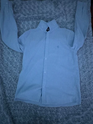 Blåvit randig skjorta från Name It. 13/14 år - Snygg blåvit randig skjorta från Name It i storlek 158-164. Skjortan har långa ärmar, klassisk krage och knappar framtill. Broderad logga på bröstet för extra detalj. Perfekt till jeans eller chinos för en clean look. Priset kan diskuteras 