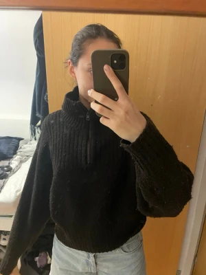 Svart stickad half zip tröja - Mysig svart stickad tröja med half zip och hög krage. Tröjan har en loose passform och långa ärmar, perfekt för kyliga dagar. Enkel att matcha med jeans eller andra byxor för en avslappnad look.