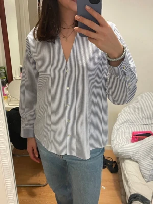 Randig skjorta från Zara i bomull - Säljer en klassisk blåvit randig skjorta från Zara i storlek S. Skjortan har lång ärm, knappar framtill och en avslappnad passform. 