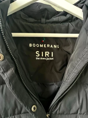 Svart dunjacka från Boomerang storlek XS  - Säljer en svart, lång dunjacka från Boomerang, modell Siri. Jackan har huva, två snedställda fickor med dragkedja och quiltad design. Perfekt för kalla dagar och har en stilren look som funkar till det mesta. Använd max 5 gånger, säljer på grund av för liten storlek. Nypris 4000. 