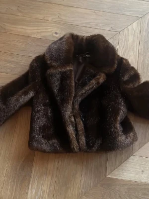 Mörkbrun pälsjacka med knappar - Bra skick genrellt. Däremot saknas en knapp dock finns en extra knapp inuti jackan. Personligen såg jag inte det inte som ett problem. Jackan har lång ärm och är fodrad på insidan. Lite osäker på storlek men passar mig som har storlek xs/s men skulle säga att det lutar mer mot xs. 