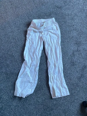 Vita linnebyxor från SRN HLT - Säljer ett par vita linnebyxor från SRN HLT med bred resår i midjan och raka ben. Byxorna har en avslappnad passform och är perfekta för varma dagar. Materialet är lätt och luftigt, vilket gör dem riktigt sköna att bära.