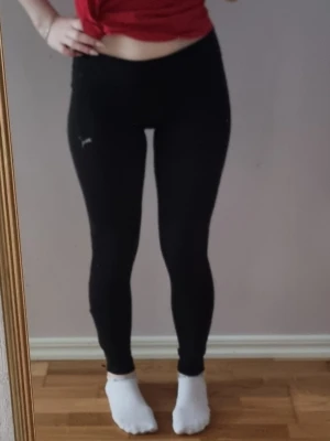 Svarta leggings från Puma med dragkedja - Säljer ett par svarta leggings från Puma med tight passform och mellan midja. Byxorna har en liten logga på låret och dragkedja vid benslutet för extra stil och funktion. Perfekta för träning eller chill dagar. Materialet är stretchigt och följsamt.
