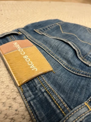 JACOB COHËNS premiumjeans limiterad utgåva i nyskick! - Limiterad utgåva av Jacob cohen, det bästa jeans märket som finns, kommer med det klassiska hästhåret och alla extradetaljer som har gjort Jacob cohen till det prestigefyllda märke som de är nu. Modellen heter bard fast och just denna färgcombination är limiterad. Nypris ligger runt 6000. Otroligt skönt material och handsydda med italienskt tyg. Finns en qr kod på som visar att de är äkta(bild 7). Pris kan diskuteras vid snabb affär!