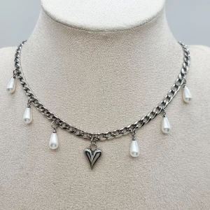 Silverhalsband med pärldroppar och hjärta - Kedjehalsband i silverfärg med fem vita droppformade pärlor och ett coolt hjärthänge i mitten. Kedjan har chunky länkar som ger en edgy vibe och pärlorna hänger snyggt längs halsen. Perfekt accessoar för att lyfta din stil.