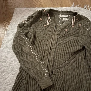 Olivgrön kofta från Odd Molly - Olivgrön stickad kofta från Odd Molly med dragkedja framtill, broderade blommor i ljusrosa och vita detaljer längs ärmar och axlar. Och figursydd. Snygg strukturstickning och ribbade muddar. Använt ca 2 gånger så väldigt bra skick!! ‼️Kan sänka priset till ett rimligt pris‼️