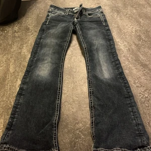 Mörkblå jeans med broderad ficka Gina Tricot - Mörkblå jeans från Gina Tricot med kontrastsömmar och snygg broderad bakficka med paljettdetaljer. Klassisk femficksmodell, dekorativ knapp framtill och bootcut-ben. Perfekta för dig som gillar detaljer och unik stil.  Knappt använd. Köpt för ca 500kr