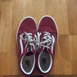 Vinröda Vans Old Skool sneakers - Säljer ett par klassiska Vans Old Skool sneakers i vinrött med vit sula och vit sidostrip. Skorna har snörning och är tillverkade i mocka och textil. Perfekta för dig som gillar streetstyle och vill ha en tidlös look. Skosnörarna är gamla men det kan man köpa nytt på skoaffärer!🩷