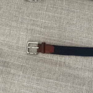 Mörkblå flätat bälte med skinn - Snyggt mörkblått flätat bälte från Selected Homme med detaljer i brunt skinn och silvrigt spänne. Perfekt accessoar för att lyfta din outfit med en klassisk och stilren touch. Bältet har en robust känsla och passar till både jeans och chinos.