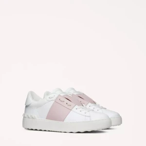 Valentino Open sneakers vit/rosa - Snygga Valentino Open sneakers i vitt skinn med en bred ljusrosa rem över mitten. Klassisk låg modell med snörning och ikoniska nitar på hälen. Perfekta för dig som vill ha en stilren men ändå unik look.