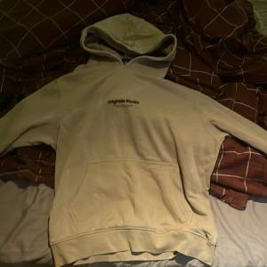 Beige hoodie från Jack & Jones - Säljer en beige hoodie från Jack & Jones Originals med tryck på bröstet. Tröjan har huva, magficka och är tillverkad i mjukt material som känns skönt mot huden. Perfekt för chill dagar och enkel att matcha med jeans eller joggers.