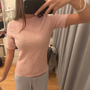 Ljusrosa ribbad topp med kort ärm - Supersöt ljusrosa topp med korta ärmar och ribbad struktur från dobber. Toppen har en lätt vågig kant vid halsen och sitter figurnära utan att vara för tight. Perfekt för dig som gillar en enkel men ändå trendig look.