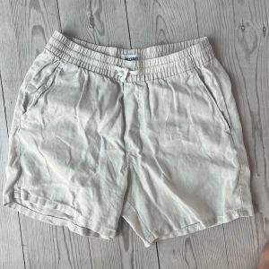 Beiga linneshorts från Weekday S - Snygga beiga linneshorts från Weekday i storlek S. Modellen har elastisk midja med snörning, två sidofickor och en bakficka. Perfekta för varma dagar med sin luftiga känsla och stilrena look.
