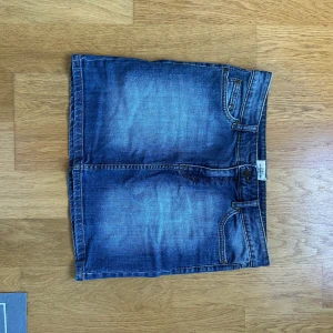 Blå jeanskjol från H&M - Snygg blå jeanskjol från H&M i klassisk femficksmodell. Kjolen är kort och har slitna detaljer samt tydliga sömmar. Perfekt för dig som gillar en avslappnad och cool stil.