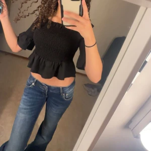 Blå bootcut jeans med låg midja - Säljer ett par blå jeans med bootcut-modell och låg midja. Jeansen har klassiska fickor fram och bak, snygga slitningar och en mörkare tvätt. Perfekta för dig som gillar en retro vibe och vill ha ett par jeans som sticker ut. Säljer även tröjan från Gina 