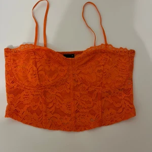 Orange spetsig topp - Säljer en orange topp med tunna axelband och vacker spets över hela plagget. Perfekt till tex neonfest💕