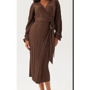 Plisserad brun omlottklänning - Snygg brun plisserad omlottklänning. Köpte den för ett specifikt tillfälle, använd endast en gång. Kommer inte till användning mer. 