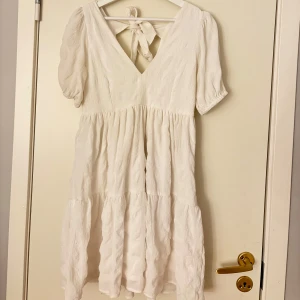 Vit kort klänning från Bubbleroom XS - Supersöt vit kort klänning från Bubbleroom med puffärmar, v-ringning och knytning i ryggen. Klänningen har volangdetaljer och är tillverkad i ett strukturerat tyg som ger en lyxig känsla. Perfekt för sommarens alla tillfällen så som student eller skolavslutning! Använd en gång!🤍🌼🎓