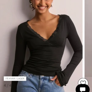 Svart omlottopp med spetsdetalj - Supersnygg svart omlottopp med v-ringning och spetskant runt halsen. Toppen har långa ärmar och sitter figurnära med en croppad känsla. Perfekt att styla med jeans eller kjol för en trendig look. Materialet känns mjukt och stretchigt.