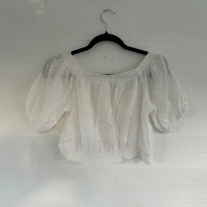 Vit broderad blus med puffärm - Superfin vit blus med broderade små blommor och puffiga korta ärmar. Toppen har smockad resår vid axlar och midja, vilket ger en snygg offshoulder-look. Perfekt för sommarens alla tillfällen och lätt att matcha med jeans eller kjol.🤩💕