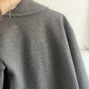 Grå skepparkavaj från Design by Si - Stilren grå skepparkavaj från Design by Si med breda slag, dubbelknäppning och klassisk passform. Jackan är fodrad och har en mjuk ullkänsla, perfekt för kyliga dagar. Snygg och tidlös modell som lyfter vilken outfit som helst.