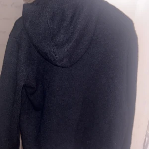 Blå stickad hoodie med huva - Mysig svart stickad hoodie med huva och långa ärmar. Perfekt för kyliga dagar och enkel att matcha med jeans eller mjukisbyxor. Tröjan har en klassisk passform och är tillverkad i ett mjukt stickat material.