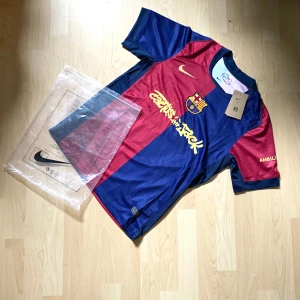 FC Barcelona Lamine Yamal matchtröja Nike - Säljer en officiell FC Barcelona matchtröja från Nike med Lamine Yamal och nummer 19 på ryggen. Tröjan är kortärmad, har klassiska blå och röda paneler, guldiga detaljer och klubbmärke på bröstet. 