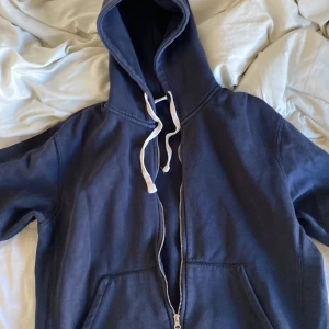 Mörkblå hoodie med dragkedja från Zara - Mörkblå hoodie från Zara i storlek L med vit snörning i huvan och hel dragkedja framtill. Tröjan har känguruficka och är tillverkad i mjukt bomullsmaterial. Perfekt för chill dagar eller när du vill ha en enkel och stilren look.