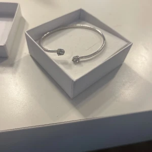 Caroline svedblom armband sliver - Snyggt och minimalistiskt armband i silverfärg med två gnistrande stenar i ändarna. Armbandet är öppet och lätt att justera runt handleden. Perfekt accessoar för att lyfta din outfit med lite extra bling.