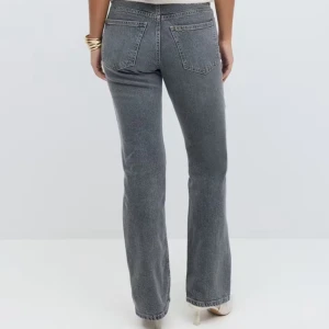 Grå bootcut jeans med hög mellan låg midja - Snygga grå jeans med bootcut passform och mellan låg midja. Klassisk femficksmodell i mjukt jeanstyg, perfekta för en chill och trendig look. Jeansen har raka ben som blir vidare nertill och stängs med knapp och dragkedja. Endast använt en gång