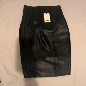 Svart skinnimitation kjol från Bik Bok - Snygg svart kortkjol i skinnimitation från Bik Bok. Kjolen har en tight passform och hög midja, vilket ger en stilren och edgy look. Perfekt att matcha med en cool topp eller oversized jacka.