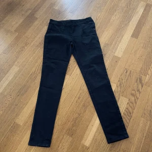 Svarta skinny byxor från Freequent - Svarta byxor från Freequent i skinny modell med hög midja och dragkedja i sidan. Snygg och enkel design som passar till det mesta. Materialet är stretchigt och bekvämt, perfekt för dig som gillar en tight passform.