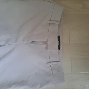 Beiga kostymbyxor från Bik Bok - Snygga beiga kostymbyxor från Bik Bok i rak modell. Byxorna har hällor för bälte och stängs med dragkedja. Perfekta för en clean och stilren look. Materialet känns mjukt och lätt, vilket gör dem bekväma att bära hela dagen.