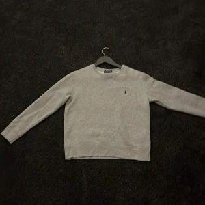 Grå sweatshirt från Polo Ralph Lauren - Säljer en stilren grå sweatshirt från Polo Ralph Lauren i storlek 10-12 år. Tröjan har lång ärm, rund halsringning och den klassiska broderade loggan på bröstet. Perfekt för dig som gillar enkel och tidlös stil.