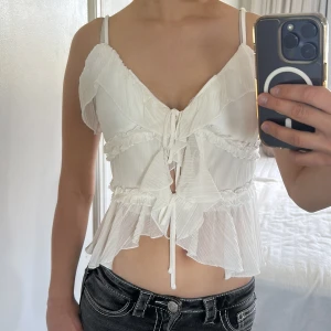 Vit volangig linnetopp med snörning - Supersöt vit linnetopp med volanger och snörning framtill.💗